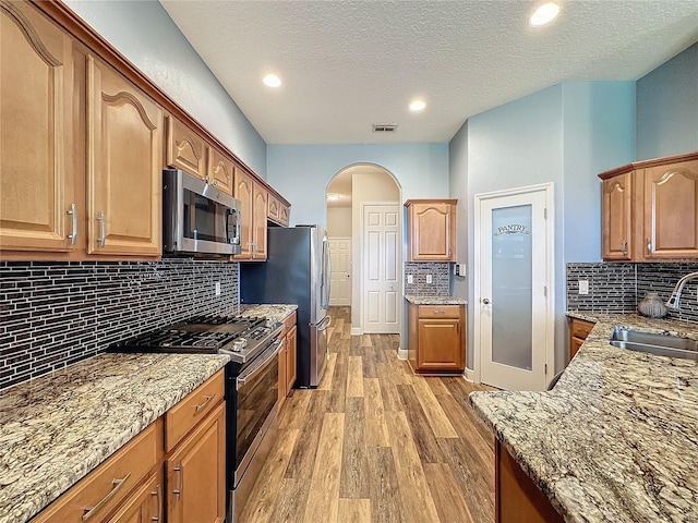 kitchen with appliances with stainless steel finishes, sink, light hardwood / wood-style flooring, light stone counters, and decorative backsplash