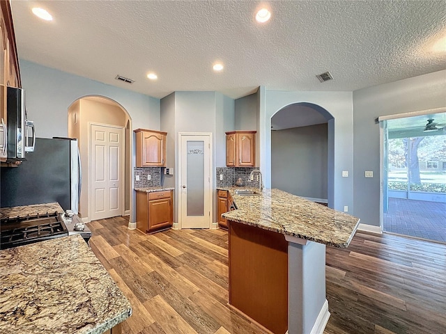 kitchen featuring wood-type flooring, sink, light stone counters, kitchen peninsula, and tasteful backsplash