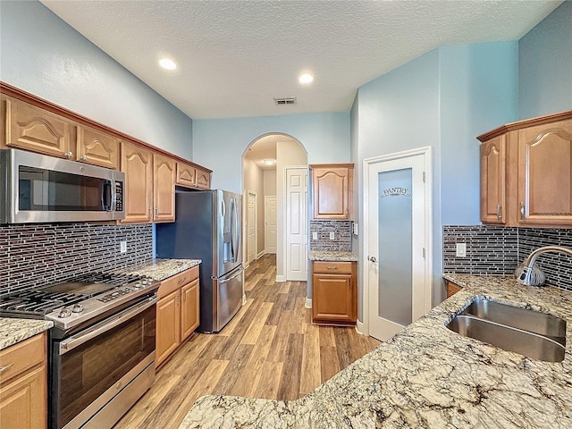 kitchen with sink, backsplash, light wood-type flooring, stainless steel appliances, and light stone countertops