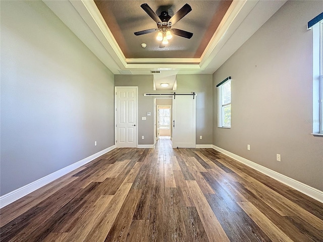 unfurnished bedroom with a tray ceiling, a barn door, and dark hardwood / wood-style floors