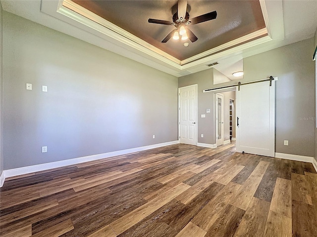 unfurnished bedroom featuring a raised ceiling, ceiling fan, a barn door, and hardwood / wood-style floors