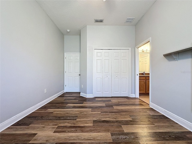 unfurnished bedroom featuring a textured ceiling, a closet, ensuite bathroom, and dark hardwood / wood-style floors