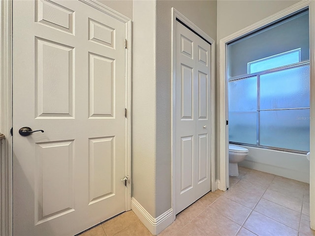 bathroom with bath / shower combo with glass door, tile patterned flooring, and toilet