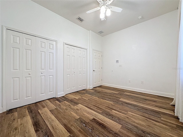 unfurnished bedroom featuring ceiling fan, two closets, and dark hardwood / wood-style flooring