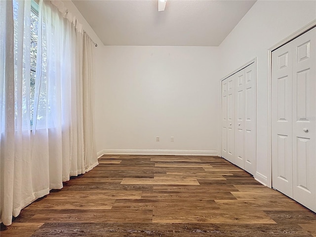 unfurnished bedroom with multiple windows, dark wood-type flooring, and two closets