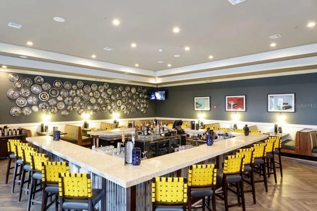 bar featuring parquet flooring, light stone countertops, and a raised ceiling