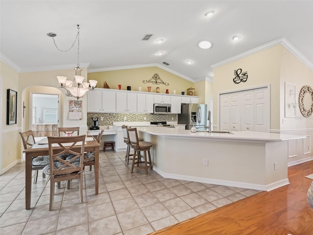 kitchen featuring white cabinets, stainless steel appliances, a center island with sink, and vaulted ceiling