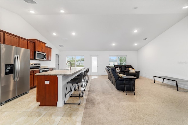 kitchen featuring a breakfast bar, sink, light carpet, appliances with stainless steel finishes, and an island with sink