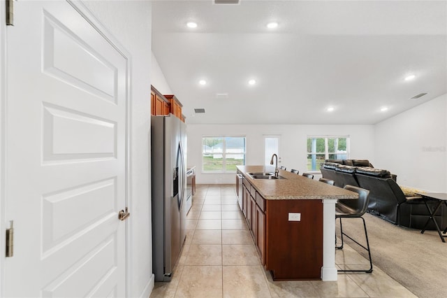 kitchen featuring sink, a kitchen breakfast bar, an island with sink, light carpet, and stainless steel fridge with ice dispenser