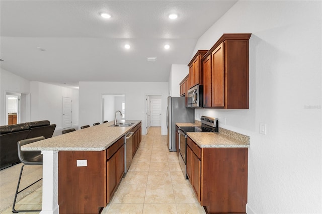 kitchen with sink, a breakfast bar, appliances with stainless steel finishes, a center island with sink, and light tile patterned flooring