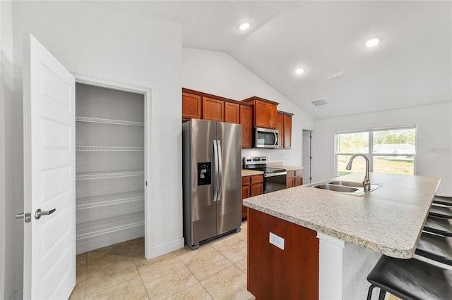 kitchen featuring sink, a breakfast bar area, stainless steel appliances, an island with sink, and vaulted ceiling