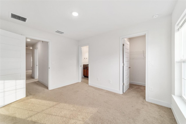 unfurnished bedroom featuring a walk in closet, light carpet, connected bathroom, and a closet