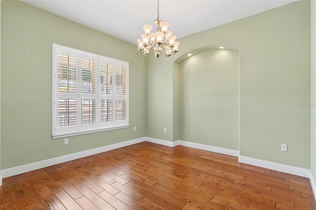 empty room with hardwood / wood-style floors and a notable chandelier