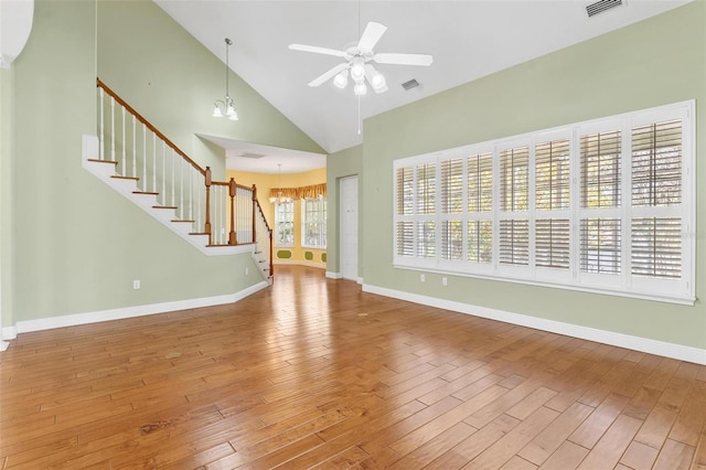 unfurnished living room with hardwood / wood-style floors, ceiling fan with notable chandelier, and high vaulted ceiling