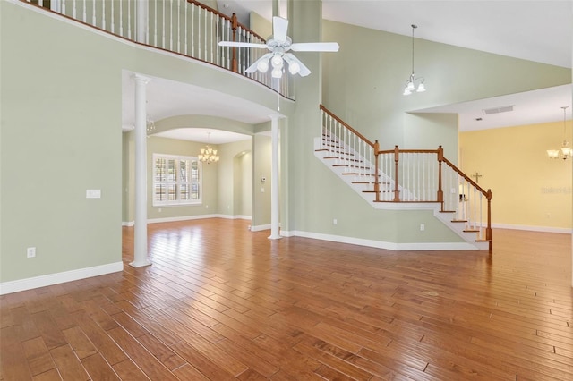 unfurnished living room featuring hardwood / wood-style floors, ceiling fan with notable chandelier, high vaulted ceiling, and ornate columns