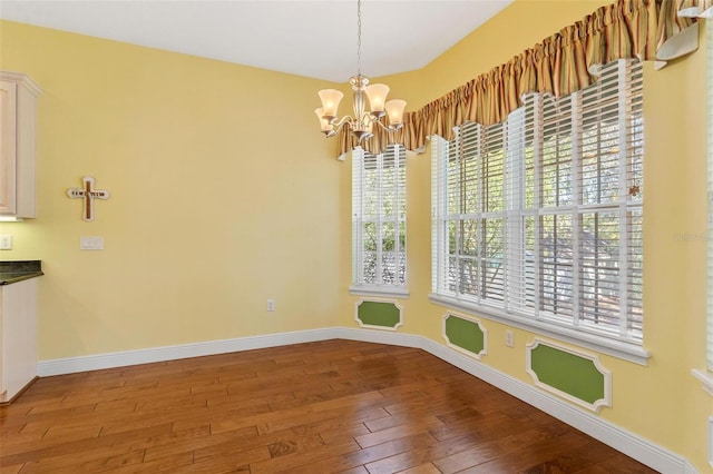 unfurnished dining area with wood-type flooring and a notable chandelier