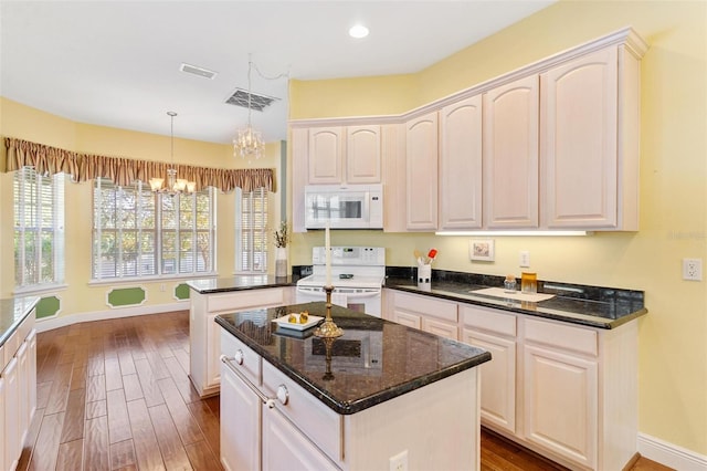 kitchen with white appliances, decorative light fixtures, dark stone counters, and a kitchen island