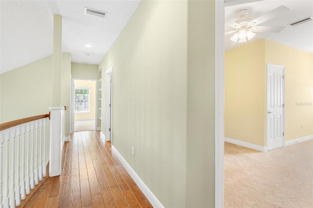 hall with lofted ceiling, light hardwood / wood-style flooring, and a textured ceiling