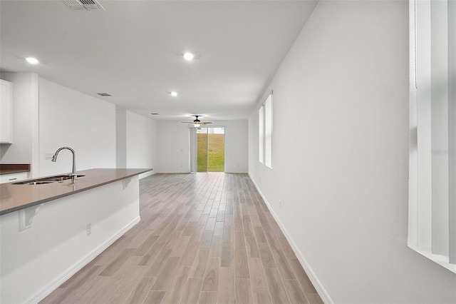 interior space with a breakfast bar, ceiling fan, sink, light hardwood / wood-style floors, and white cabinetry