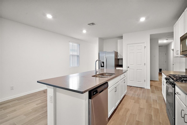 kitchen with stainless steel appliances, a kitchen island with sink, sink, white cabinets, and light hardwood / wood-style floors