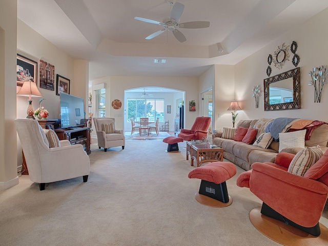 carpeted living room with ceiling fan and a tray ceiling