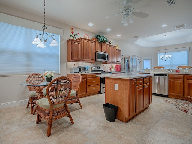 kitchen with stainless steel appliances, pendant lighting, ceiling fan with notable chandelier, and a kitchen island