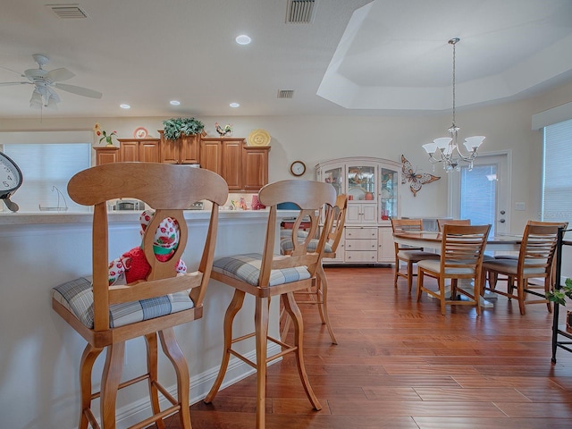 dining area featuring ceiling fan with notable chandelier, wood-type flooring, and a tray ceiling