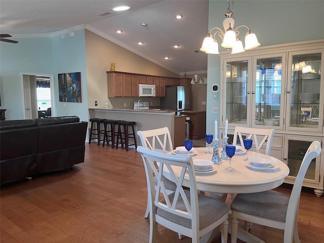 dining space with lofted ceiling, ceiling fan with notable chandelier, wood finished floors, visible vents, and ornamental molding