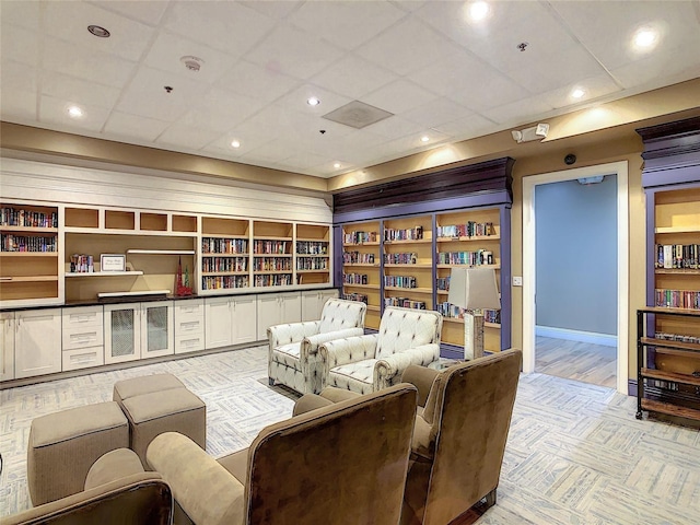 carpeted living room featuring built in features and a drop ceiling