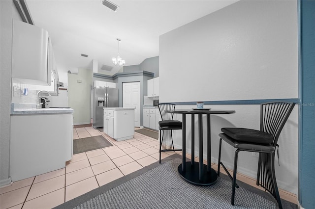 kitchen with a center island, stainless steel refrigerator with ice dispenser, light tile patterned floors, visible vents, and white cabinetry