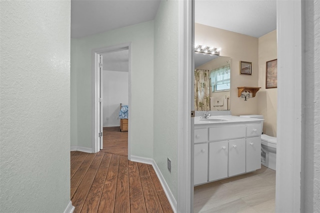 bathroom featuring a textured wall, toilet, vanity, wood finished floors, and baseboards