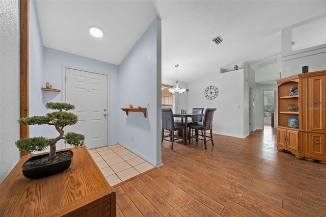 foyer with a wealth of natural light, a notable chandelier, vaulted ceiling, and wood finished floors