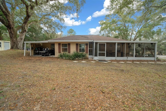 back of house featuring a sunroom, an attached carport, and stucco siding