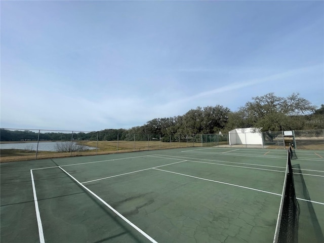 view of tennis court with a water view and fence