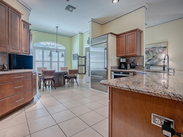 kitchen featuring tasteful backsplash, pendant lighting, sink, light stone counters, and built in fridge