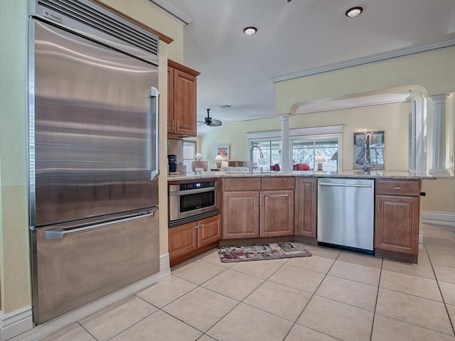 kitchen with appliances with stainless steel finishes, sink, kitchen peninsula, light tile patterned flooring, and light stone counters