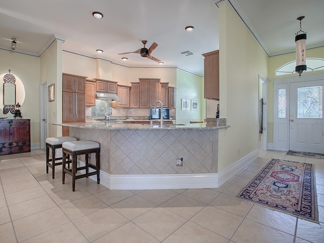 kitchen featuring light tile patterned floors, kitchen peninsula, ceiling fan, a kitchen breakfast bar, and ornamental molding