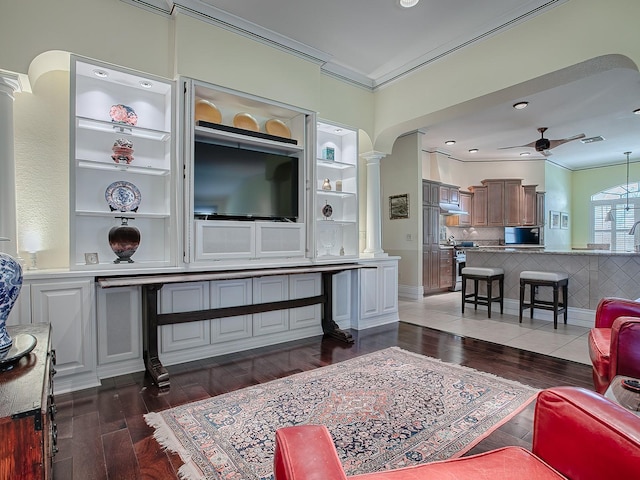 living room with dark wood-type flooring, ornate columns, crown molding, and ceiling fan