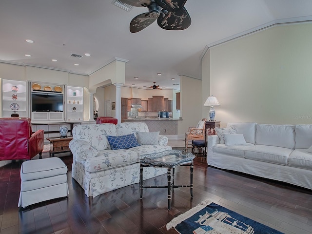 living room with ceiling fan, dark wood-type flooring, crown molding, and ornate columns