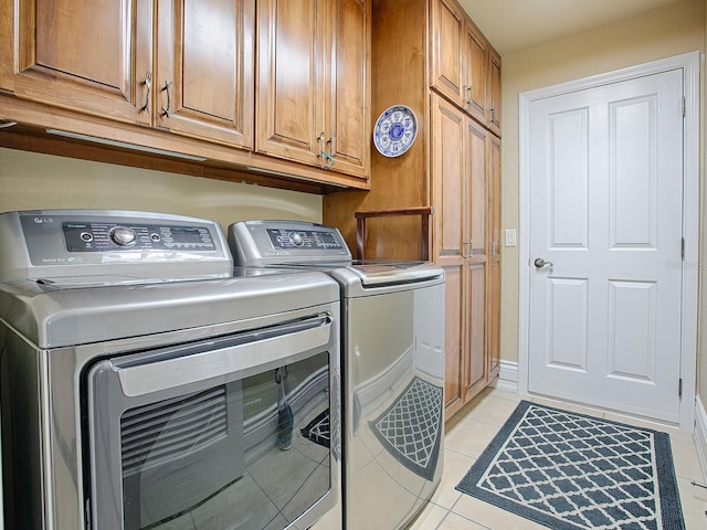 clothes washing area with washer and dryer, cabinets, and light tile patterned floors