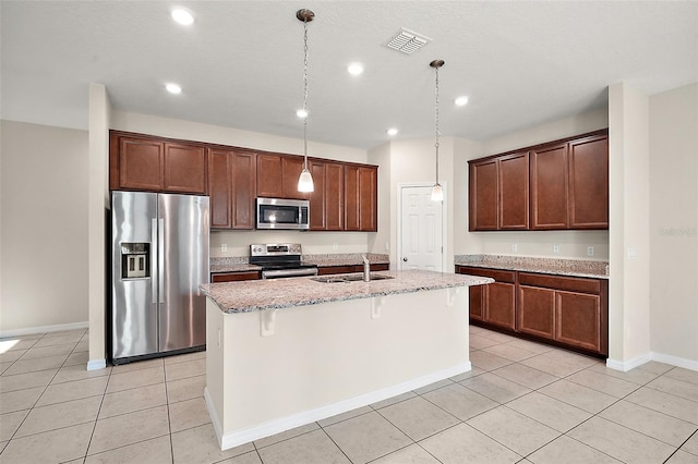 kitchen featuring appliances with stainless steel finishes, decorative light fixtures, a breakfast bar area, light tile patterned floors, and a center island with sink