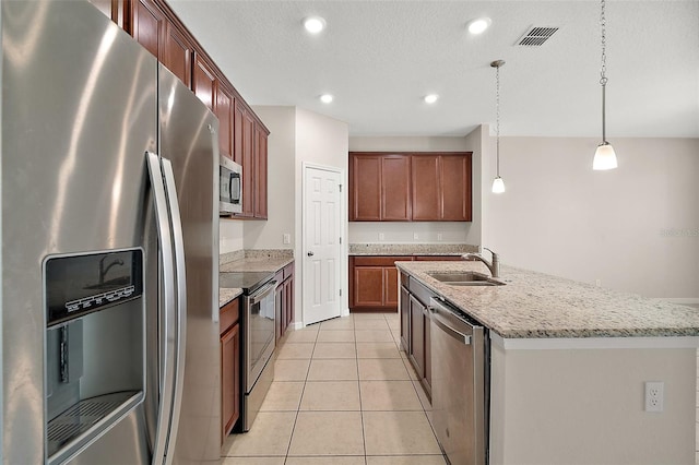 kitchen featuring pendant lighting, sink, light tile patterned floors, stainless steel appliances, and a center island with sink