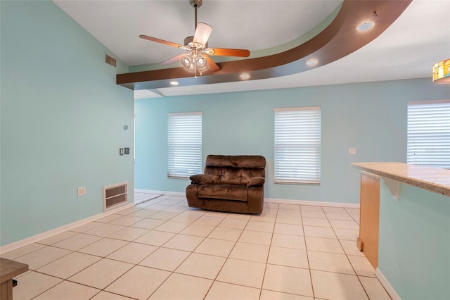 sitting room with a raised ceiling, light tile patterned flooring, and ceiling fan