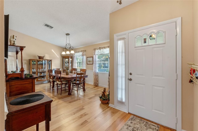 foyer entrance featuring a textured ceiling, an inviting chandelier, and light hardwood / wood-style flooring