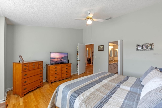 bedroom featuring a textured ceiling, a towering ceiling, ceiling fan, ensuite bathroom, and light hardwood / wood-style flooring