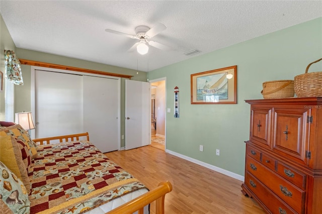 bedroom featuring ceiling fan, a closet, light wood-type flooring, and a textured ceiling