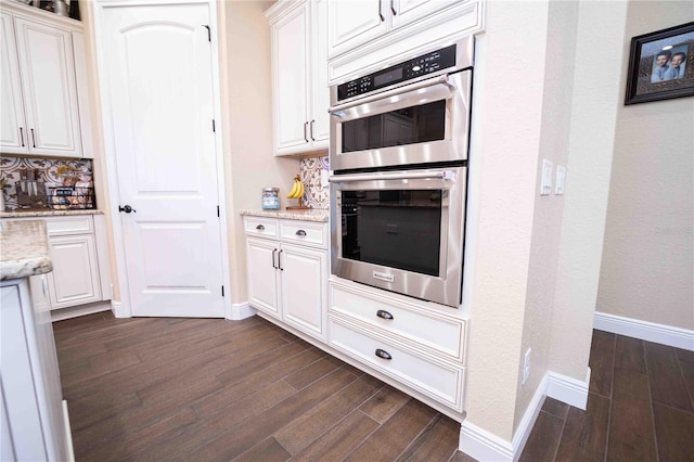 kitchen with stainless steel double oven, light stone countertops, dark hardwood / wood-style flooring, and white cabinetry