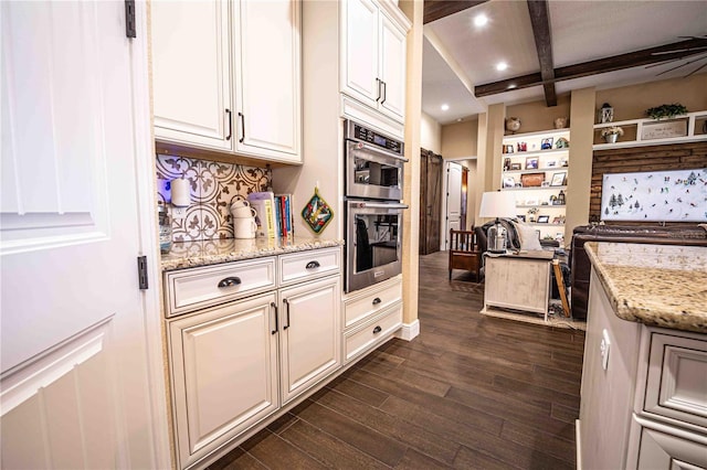 kitchen featuring white cabinets, light stone counters, beamed ceiling, stainless steel double oven, and dark hardwood / wood-style floors