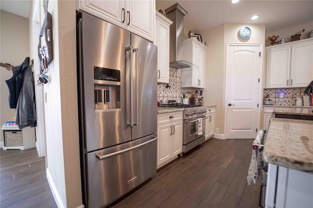 kitchen featuring wall chimney exhaust hood, white cabinetry, light stone countertops, and premium appliances