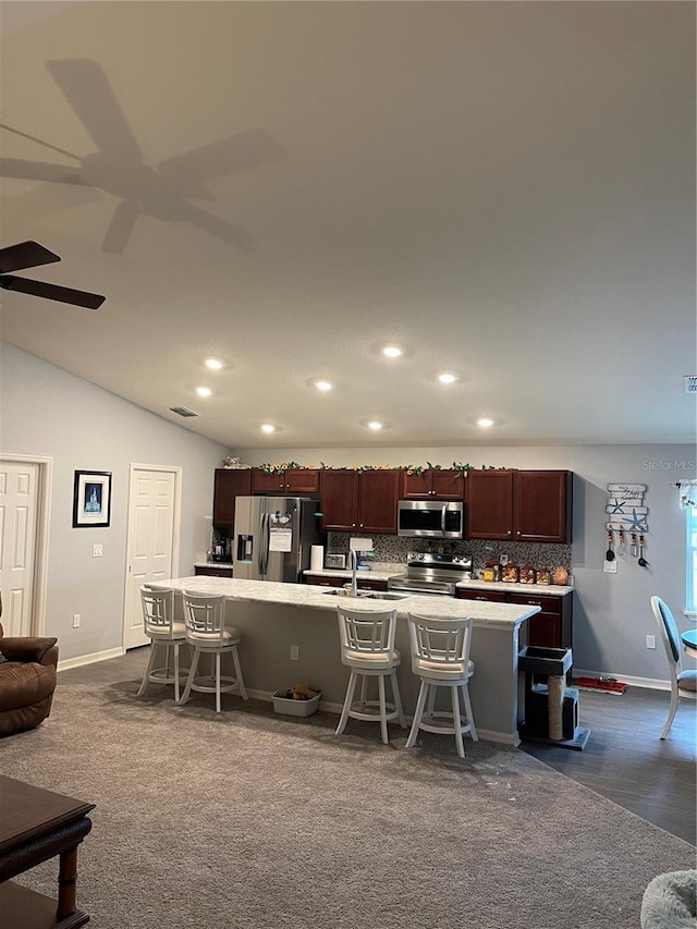 kitchen featuring a kitchen breakfast bar, appliances with stainless steel finishes, a kitchen island with sink, and lofted ceiling